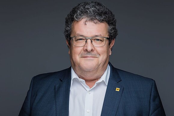 Klaus Höckner vertritt Österreich im neuen EU-Center AccessibleEU für Barrierefreiheit. Foto: Studio Mat. Mann mit weißem Hemd, blauem Sakko, Brille und dunklen kurzen Locken lächelt in die Kamera vor schwarzem Hintergrund