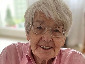 Eva Seefranz Porträt von Dame mit weißen Haaren und Brille in rosa Bluse, die in die Kamera blickt.