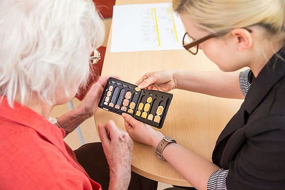 Wir finden das passende Hilfsmittel für Sie. Copyright: Franz Pfluegl Eine Mitarbeiterin zeigt einem Mitglied einen Euro-Münzsortierer.