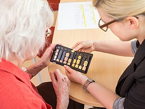 Wir finden das passende Hilfsmittel für Sie. Copyright: Franz Pfluegl Eine Mitarbeiterin zeigt einem Mitglied einen Euro-Münzsortierer.