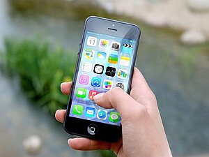 Schwarzes iPhone in der Hand, Screen zeigt viele Apps. 