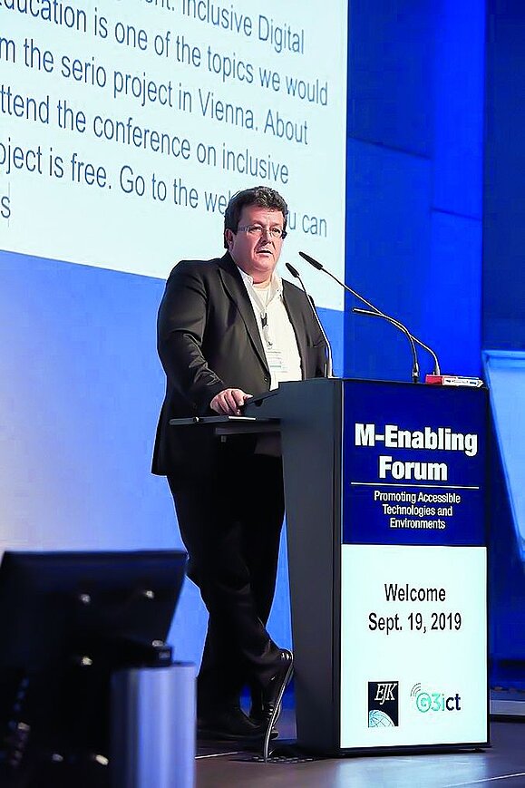 Klaus Höckner ist ein gefragter Experte, hier bei einem Vortrag beim M-Enabling Forum. Mann mit Anzug vor Leinwand am Rednerpult.