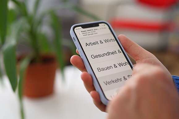 Blue_Beanie_Day_-_Gesetz_digitale_Barrierefreiheit_kommt.jpg Smartphone Nahaufnahme mit starkem Zoom auf Begriffe: Arbeit, Gesundheit, Bauen