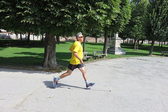 Laufen kann man auch mit Sehbehinderung, zeigt unsere Laufgruppe. Laufender Mann mit gelbem T-Shirt und weißem Stock in der Hand