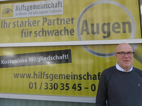 Mitarbeiter Daniele M. steht vor einem gelbschwarzen Plakat der Hilfsgemeinschaft