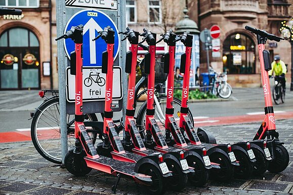 mehrere rote E-Scooter mit Aufschrift "VOI" ordentlich nebeneinandergeparkt