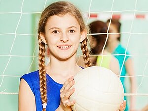 Mädchen mit Volleyball. Ein Teenager-Mädchen in blauem, ärmellosen Shirt und mit Zöpfen, hält einen Volleyball in die Höhe.