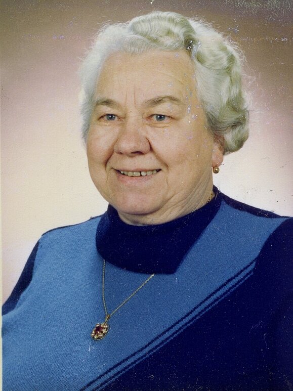 Maria Tucek Eine ältere Dame mit weißer Dauerwelle lächelt freundlich, sie blickt an der Kamera vorbei