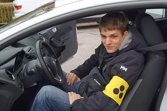 Ein blinder junger Mann sitzt in einem Auto auf dem Fahrersitz
