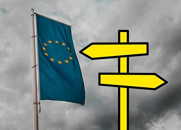 Flagge der EU, daneben ein Wegweiser, der in verschiedene Richtungen zeigt. 