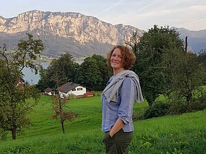 Eine Frau steht auf einem Hügel und blickt auf einem See mit dahinterliegender Bergkette.