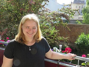 Die sehbehinderte Bettina F. steht auf ihrem Balkon in der Sonne und lächelt. Foto: Die sehbehinderte Bettina F. steht auf ihrem Balkon in der Sonne und lächelt