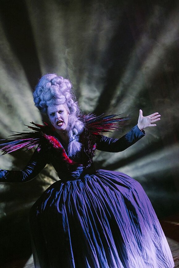 verkleidete pompöse Frau mit weißer Perücke und weiß gepudertem Gesicht, pompöses Kleid, dahinter Scheinwerfer