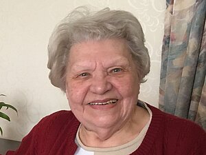 Anna Huber hatte selbst eine Sehbehinderung. Ältere Frau mit grauen Haaren und weinroter Jacke lächelt in die Kamera