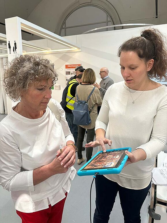 Frau zeigt anderer Frau ein Tablet mit taktilem Relief.