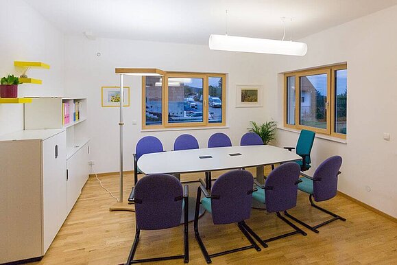 Tischbeleuchtung mittels Steh- und Pendelleuchte, Copyright: VIDEBIS Ein Besprechungsraum der mit einer Stehleuchte und einer rohrförmigen Deckenleuchte beleuchtet wird